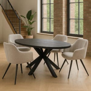 Zwarte ovale mangohouten eettafel met kruisvormige metalen poot, omringd door vier beige gestoffeerde eetstoelen in een moderne, lichte woonruimte met houten vloer en grote ramen.