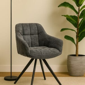 Eetkamerstoel in grijs antraciet ribstof met armleuningen en 180 graden draaifunctie op een zwart metalen spinpoot, geplaatst in een modern interieur met vloerlamp en kamerplant.